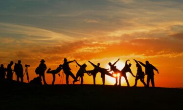 Group of people silhouetted against a vibrant sunset, showcasing unity and joy.