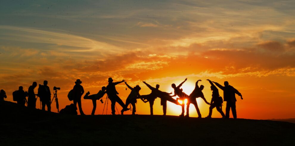 Group of people silhouetted against a vibrant sunset, showcasing unity and joy.